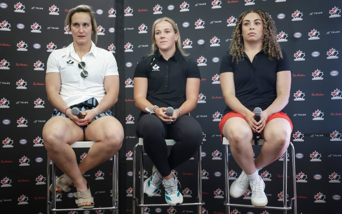 Three women sit on stools, holding microphones.