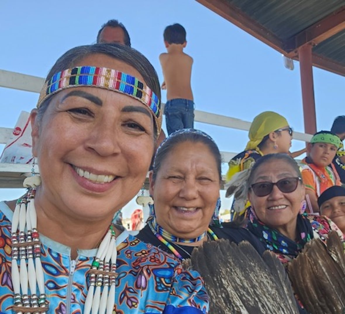 Three women pose in dresses that have tin cones attached to them, one woman in the middle had a beaded headband and sunglasses.