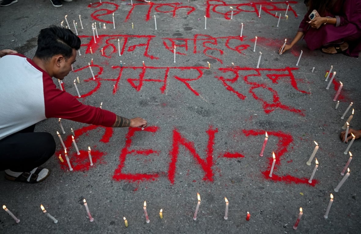 A man touches the floor alongside writing on the walls, with Gen Z words, surrounded by candles.
