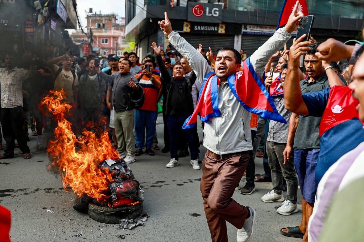 A man stands with Nepalese on his neck and a burning frame can be seen.