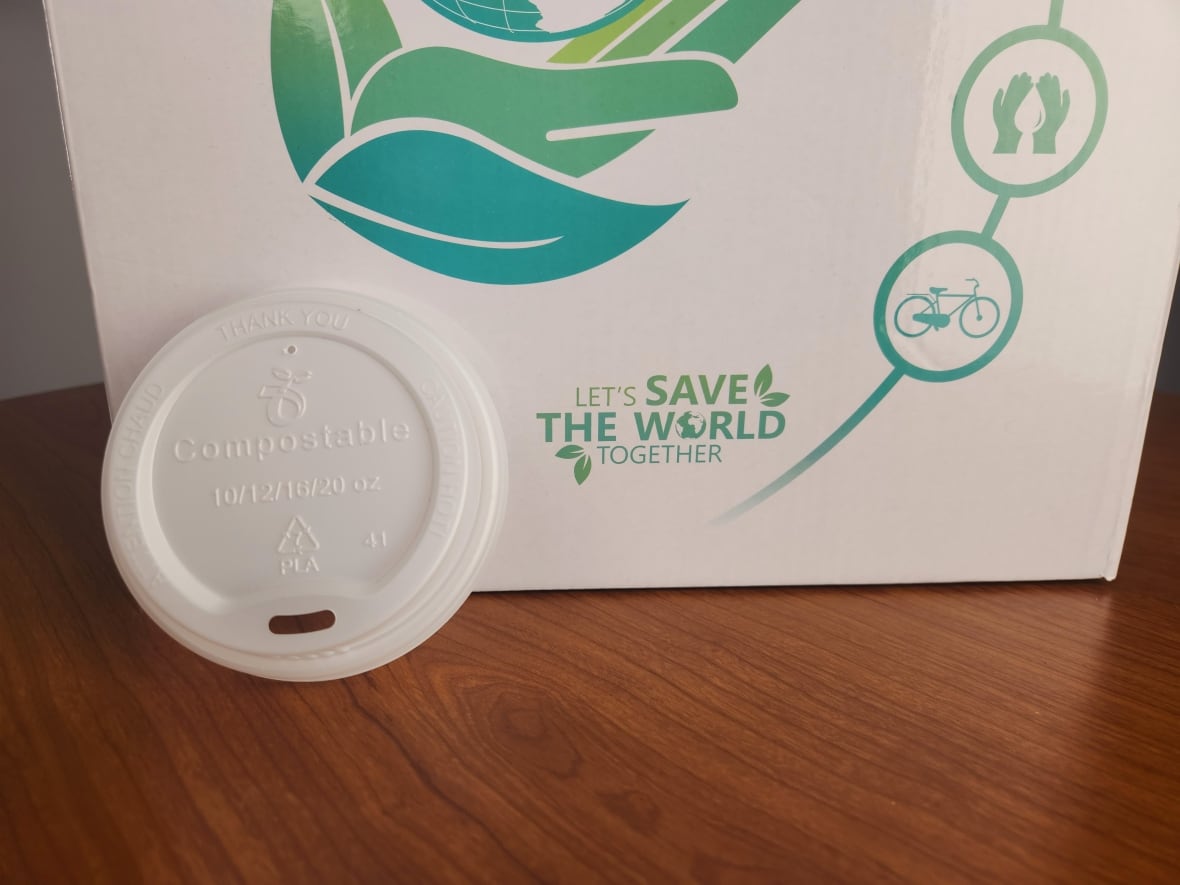Uma tampa de café de plástico se inclina contra algumas embalagens compostáveis.