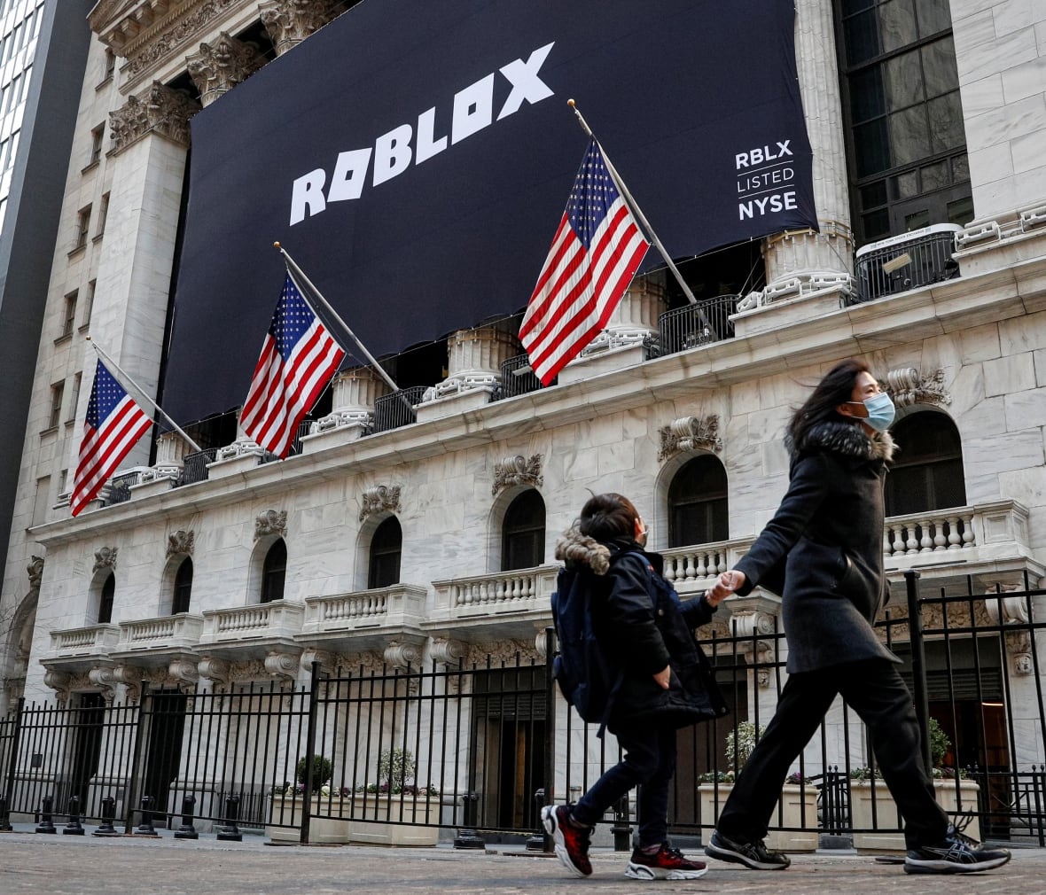 A child looks back at a banner for Roblox, displayed to celebrate the company's IPO, on the front facade of an ornate building.