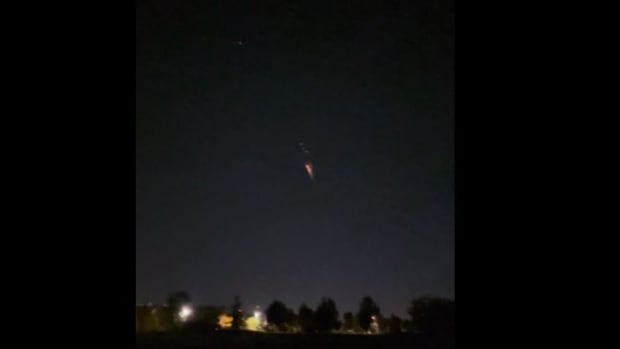 A blurry screen grab shows a fiery ball in the night sky above the city treeline. 