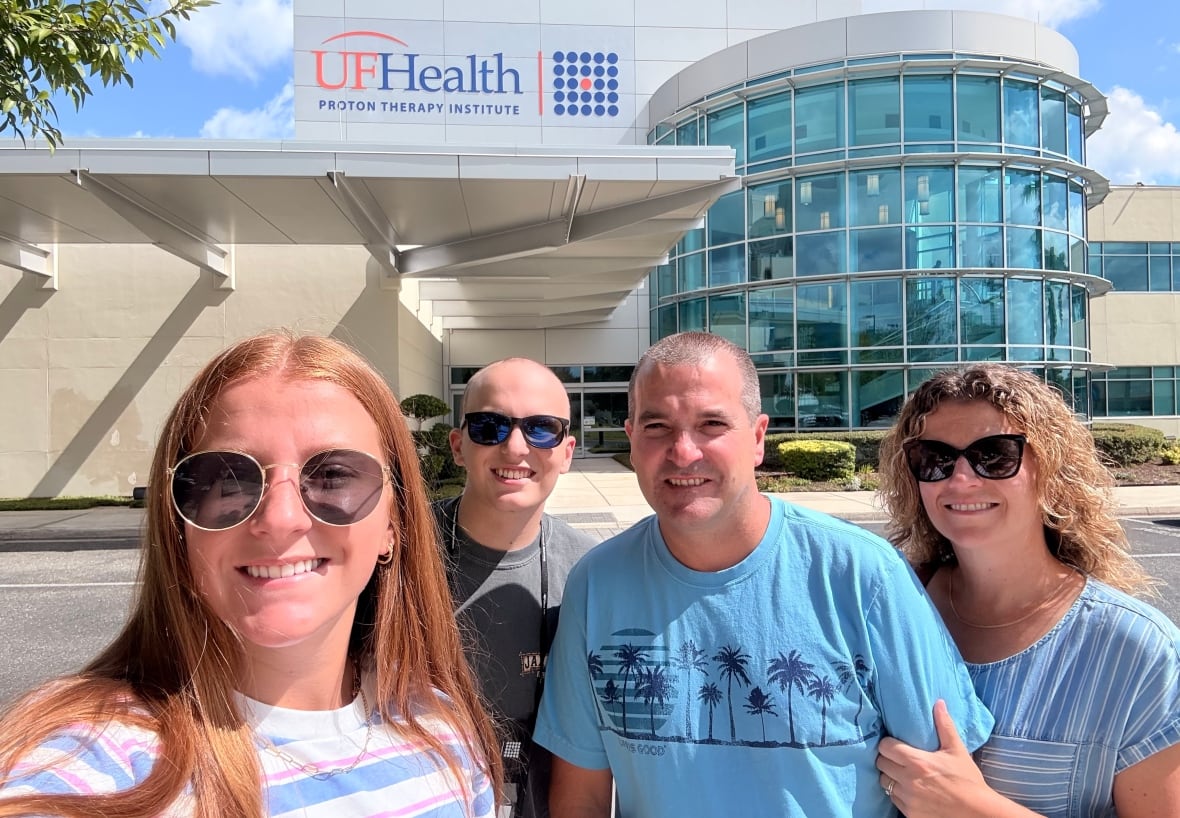 Una famiglia di quattro persone dell'Ontario posa per una foto davanti all'edificio dell'UF Health Proton Therapy Institute in Florida.
