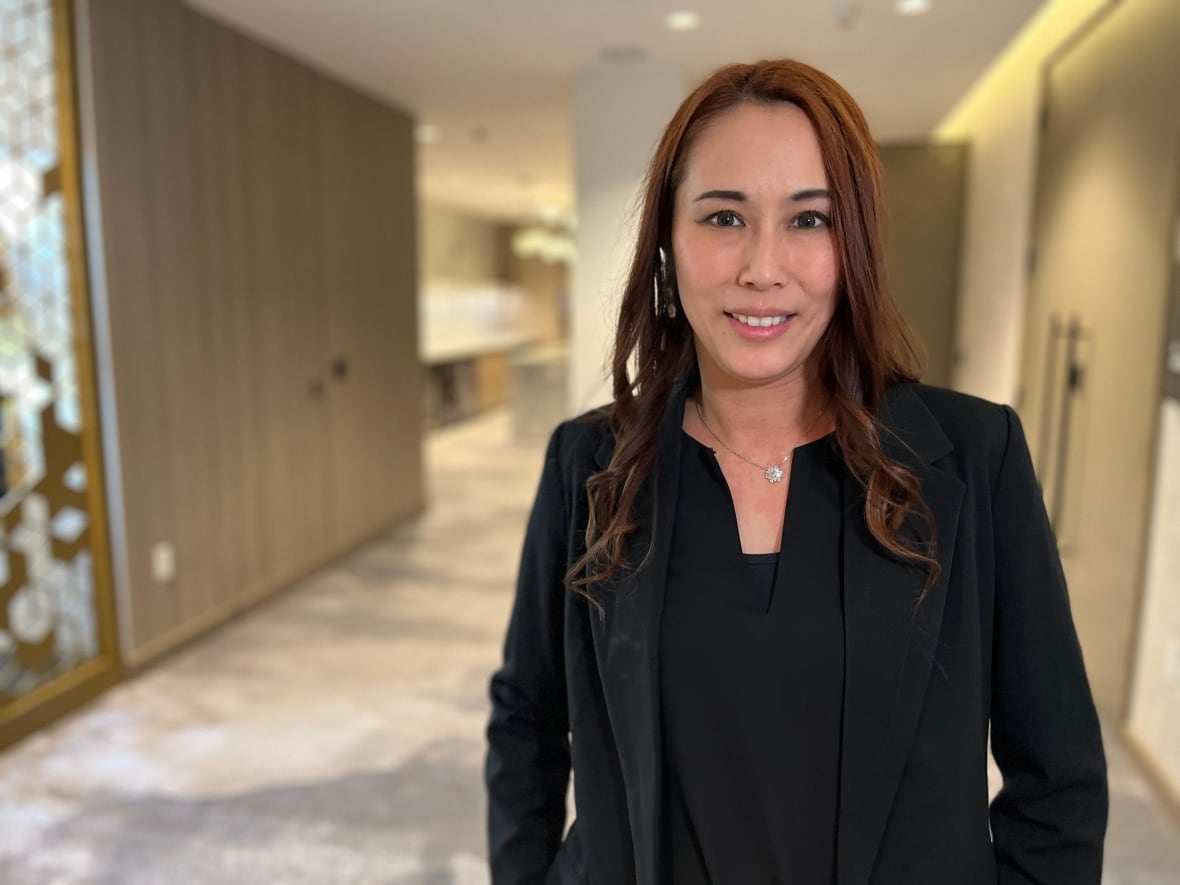 A woman in a black suit jacket and blouse stands in a hallway outside a hotel boardroom.