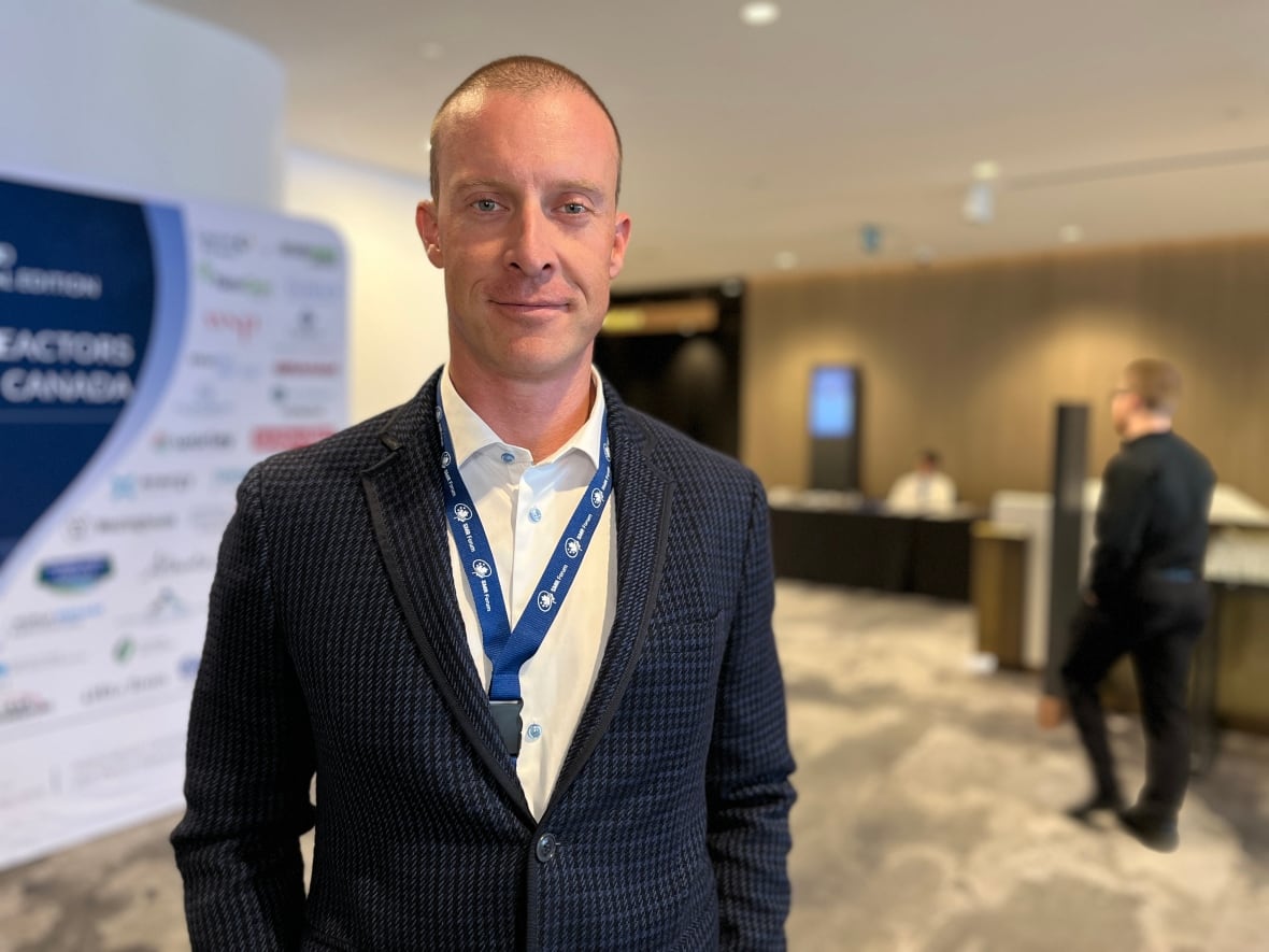 A man wearing a blue suit jacket, white shirt and conference lanyard poses for a photo in front of a sign promoting the SMR Forum.