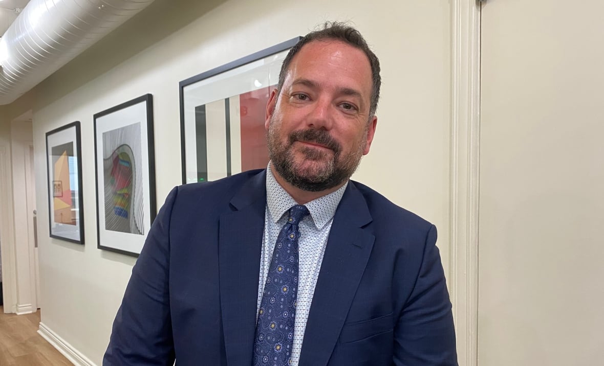 Adam Weisberg wearing a suit standing in front of a wall with some artwork on it. 