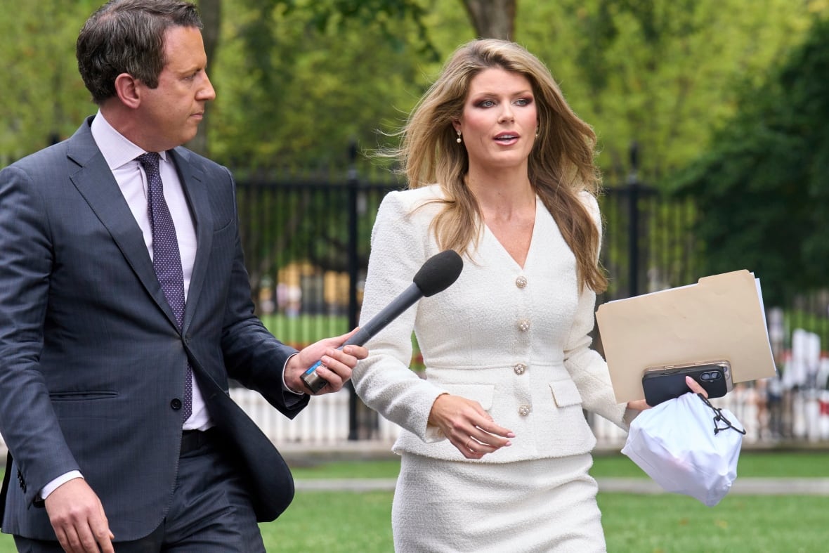 A man wearing a suit walking and carrying a microphone for a woman wearing a white suit 