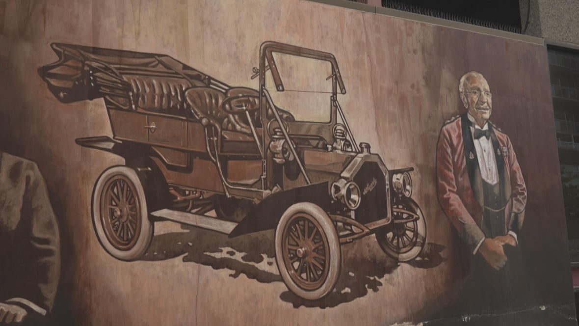Photo of a painted mural showing an old fashioned car and a man standing next to it. 