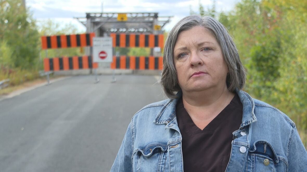Woman in jean jacket stands in front of barricaded bridge. 