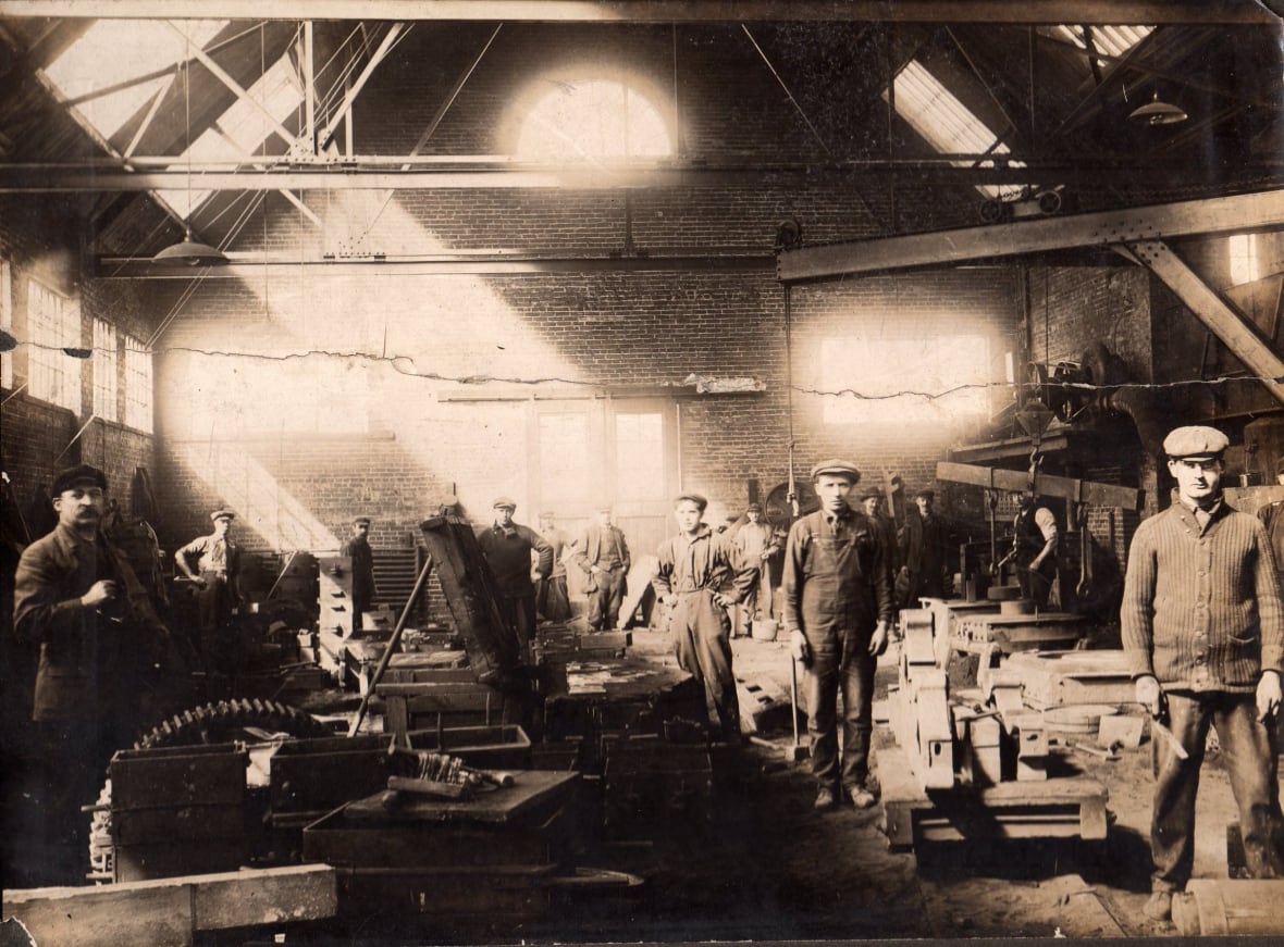 Black and white historic photo showing several workers inside a car plant. 