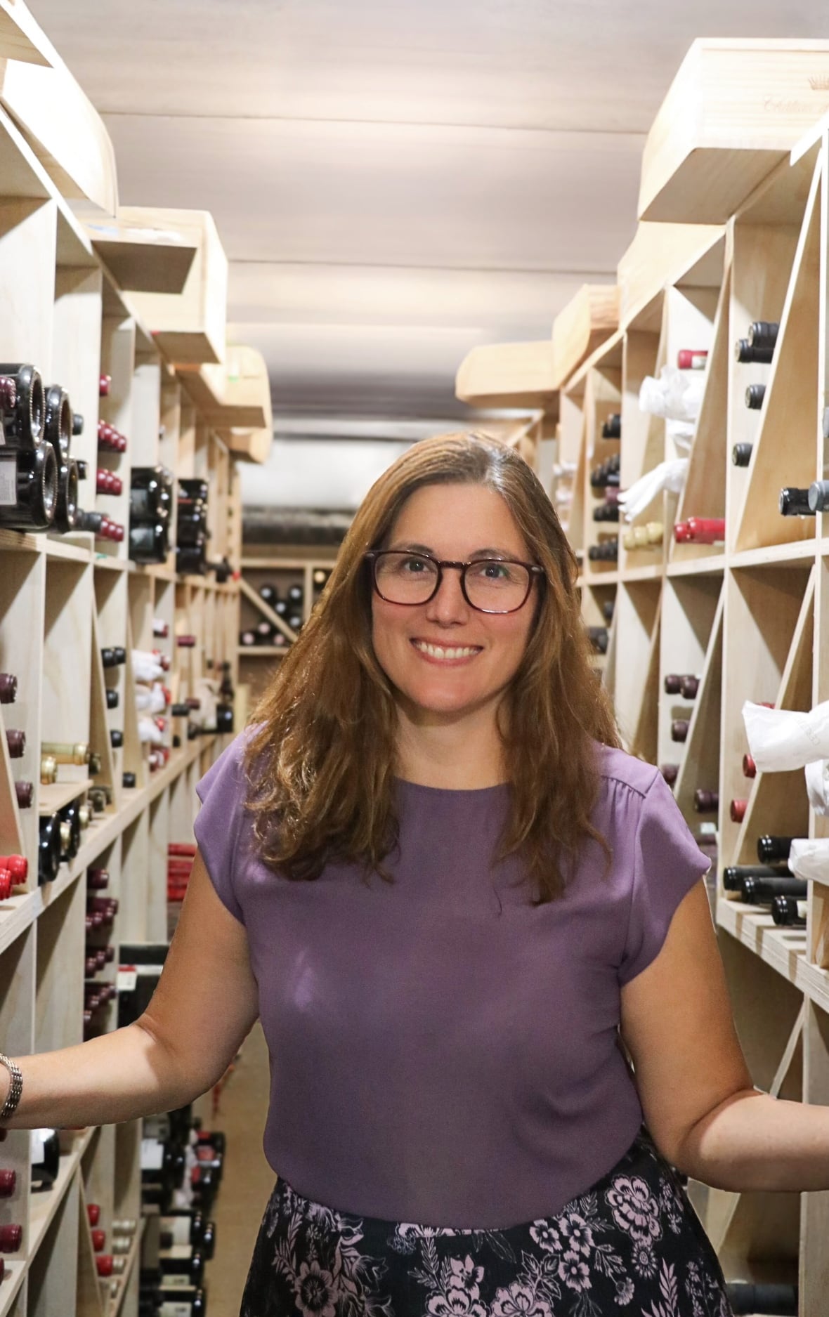 A woman stands in a wine cellar.