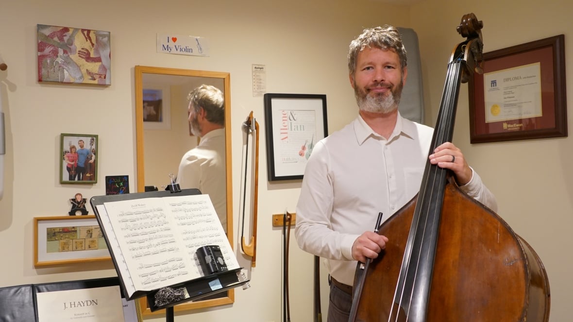 A man stands in a room with a mirror holding a bass.