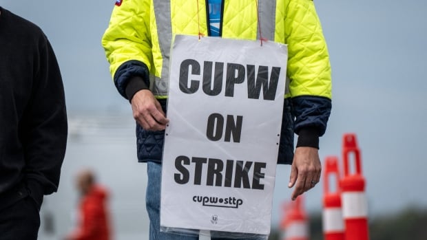 A closeup shows a person in a yellow jacket with a sign reading "CUPW on strike."