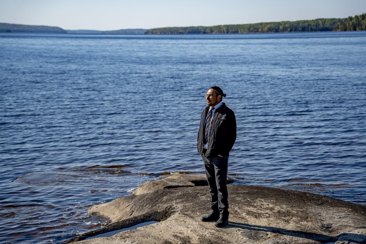 A person is seen standing on a rock on the water.