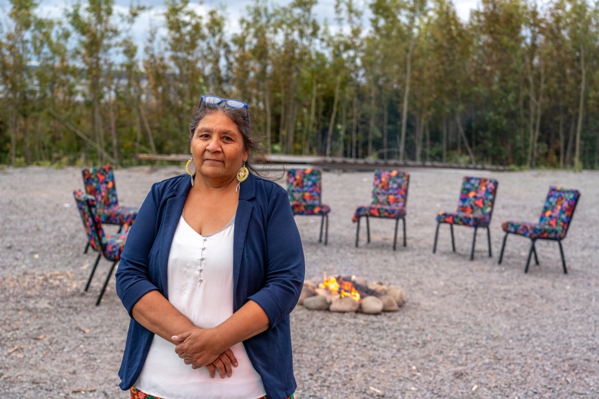 A person is seen standing outside in front of a fire pit surrounded by chairs.