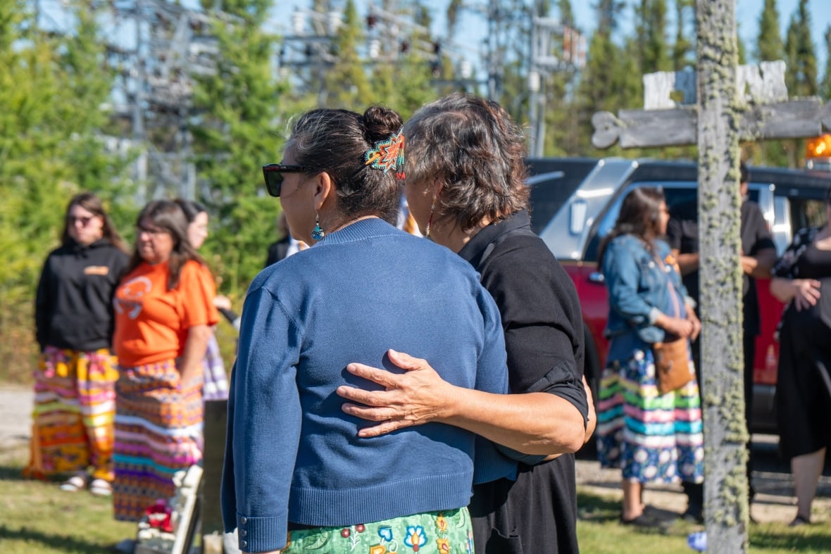Two people are seen from behind with their arms around each other.
