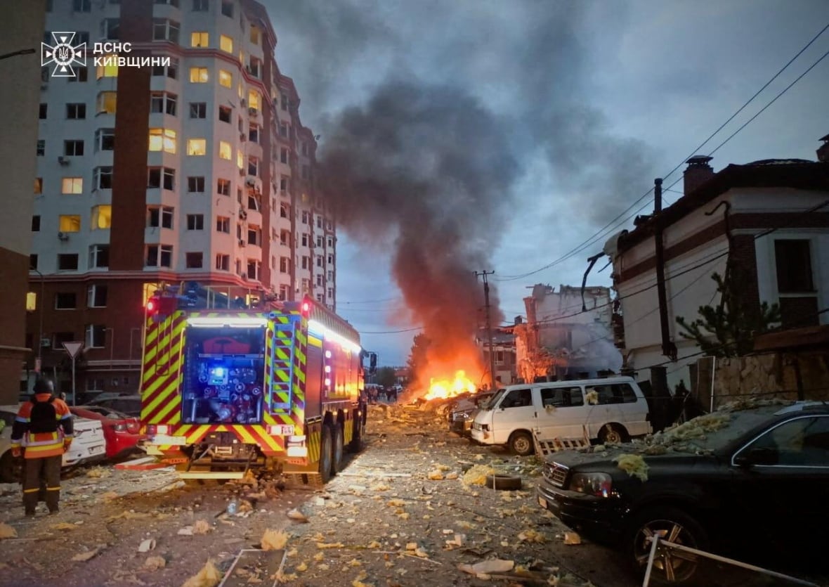 A ball of fire is seen at the end of the street lined with destroyed buildings and an ambulance. 