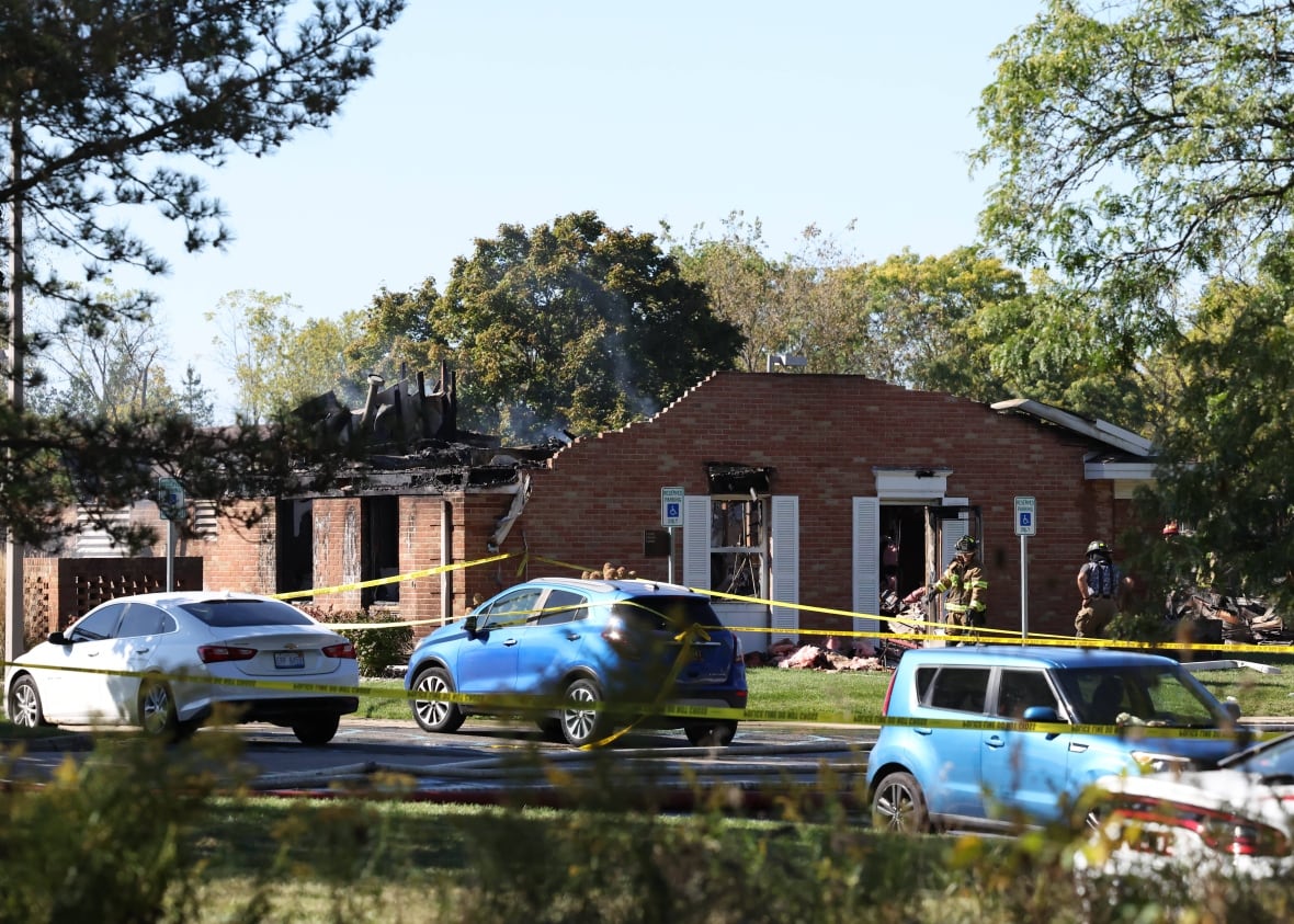 Fire and law enforcement officers stand outside a burned roof.