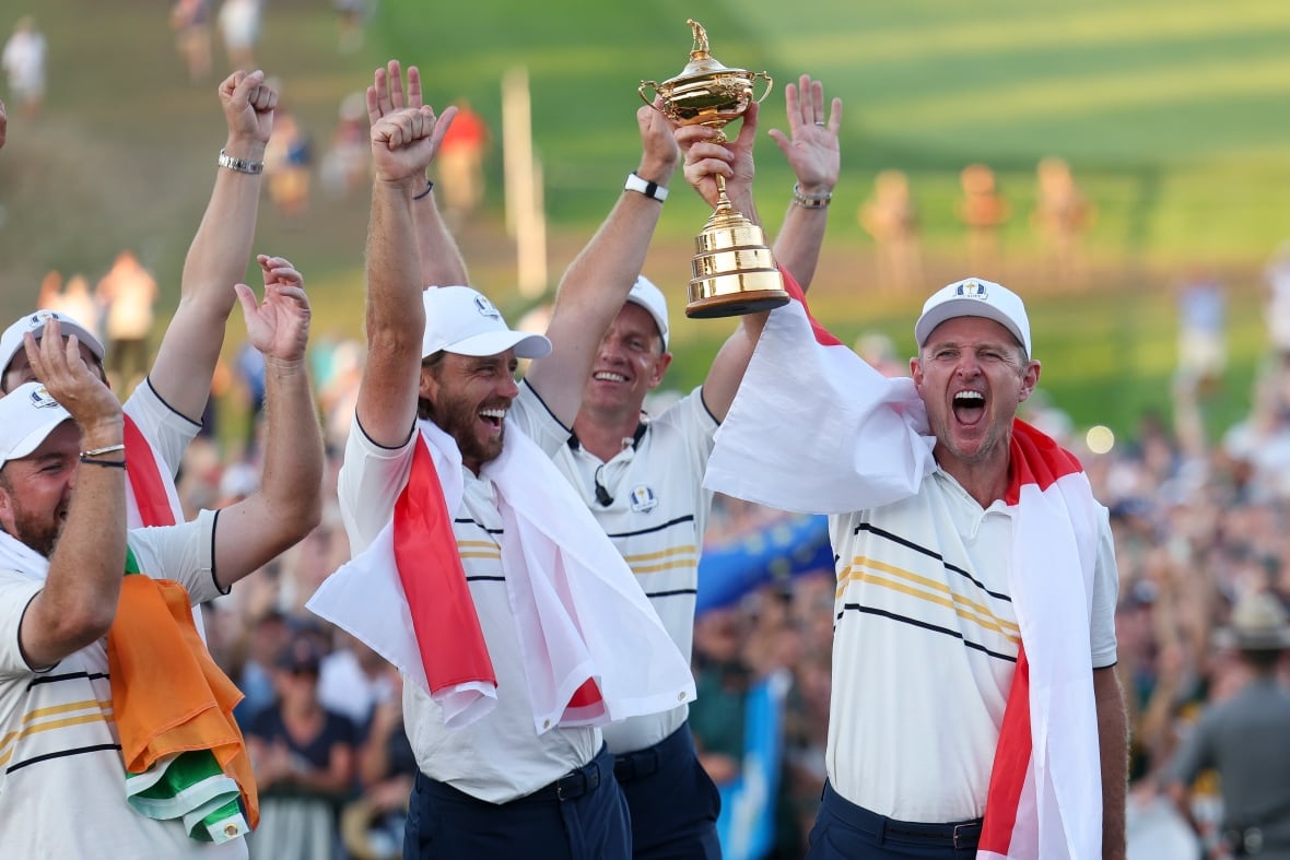 A group of golfers draped in flags hold a trophy.