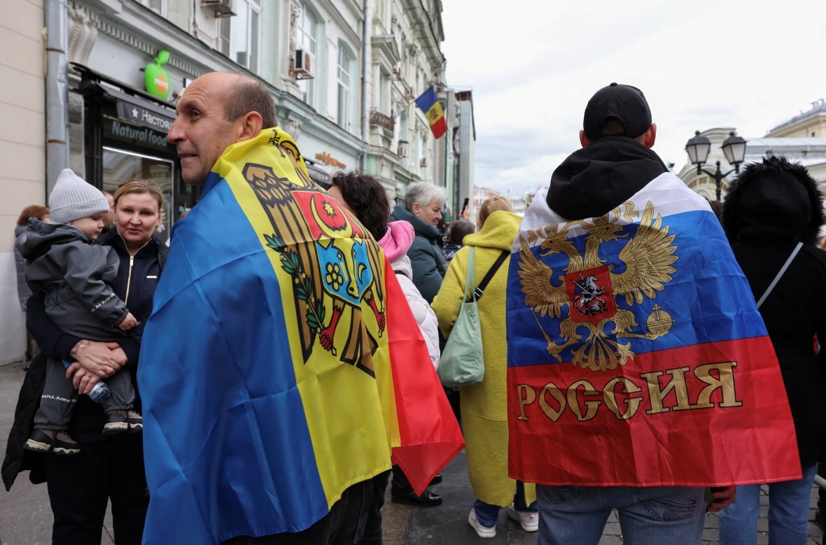 Two people, while appearing to the camera, wear their backs while many people stand abroad.