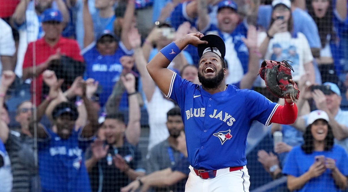 A baseball player raises his cap in celebration in front of a backdrop of fans at a stadium.