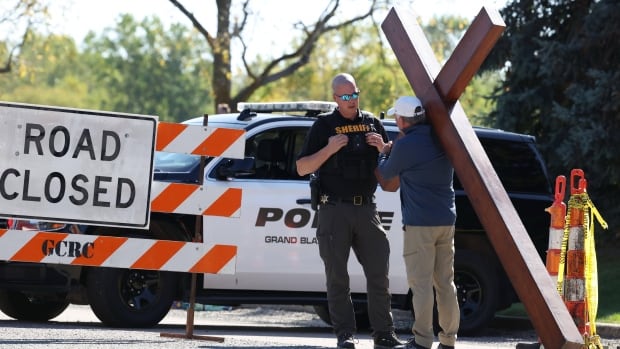 Dan Beazley, carrying his 10-foot-cross, is stopped by a sheriff's deputy near the Church of Jesus Christ of Latter-day Saints, Monday, Sept. 29, 2025 in Grand Blanc Township, Mich.
