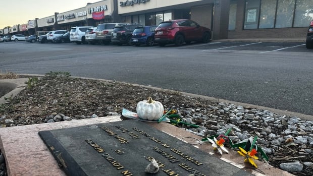 A photo shows the ground in a strip mall parking lot, with a memorial plaque.