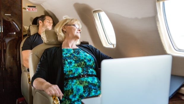 A man and a woman on a plane lean back in their seats and sleep