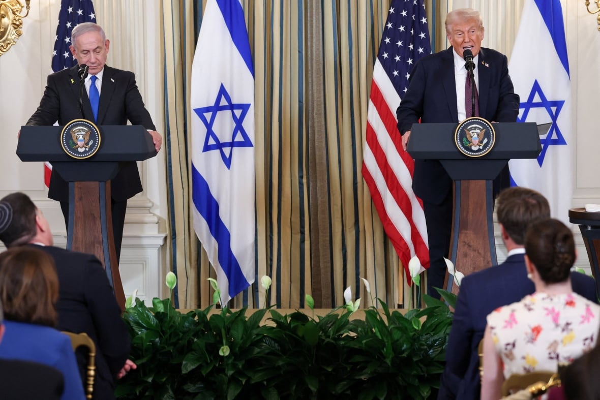 Two men stand in the lecturers. There are American and Israeli flags in the background.