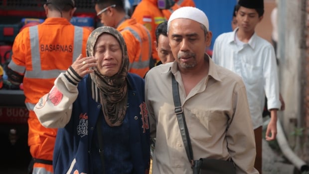 A man and woman, both crying, with rescue workers behind them