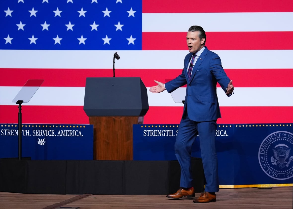 A man who wears a suit in front of a giant American flag speaks