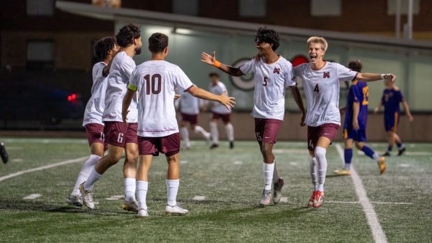 Five soccer players in matching uniforms come together to high five on a field at night.