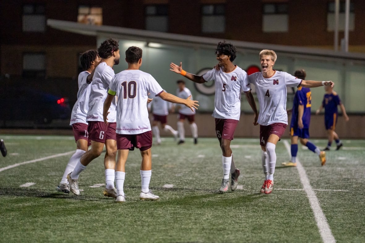 Five soccer players in matching uniforms come together to high five on a field at night.