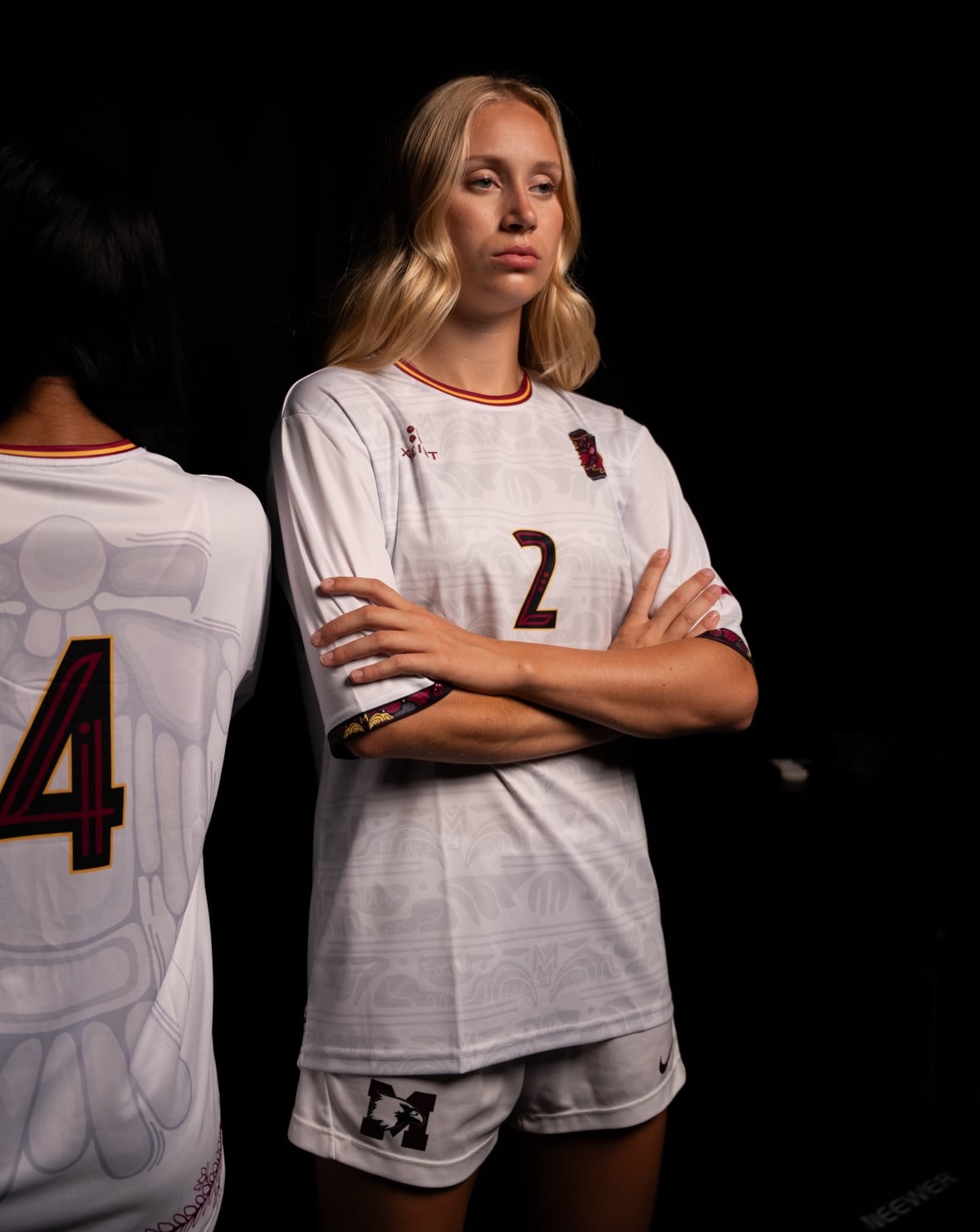 A person in a sports uniform poses against a black backdrop. To the left, another person poses facing away from the camera.