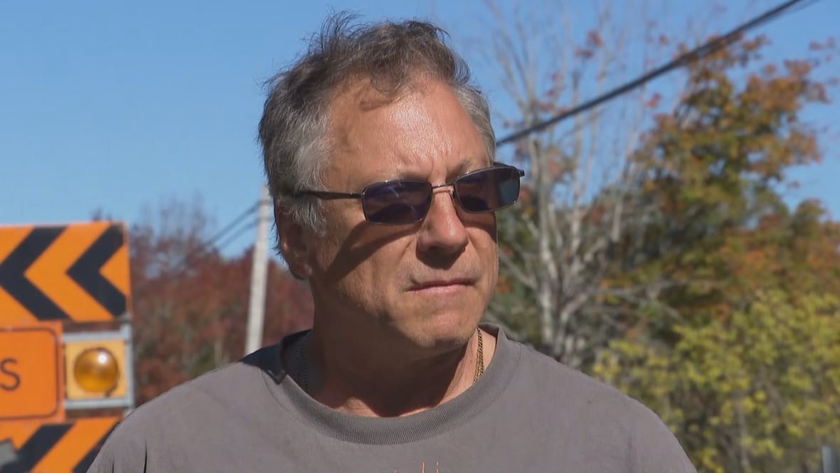 A man wearing sunglasses stands outside in front of a construction barrier.