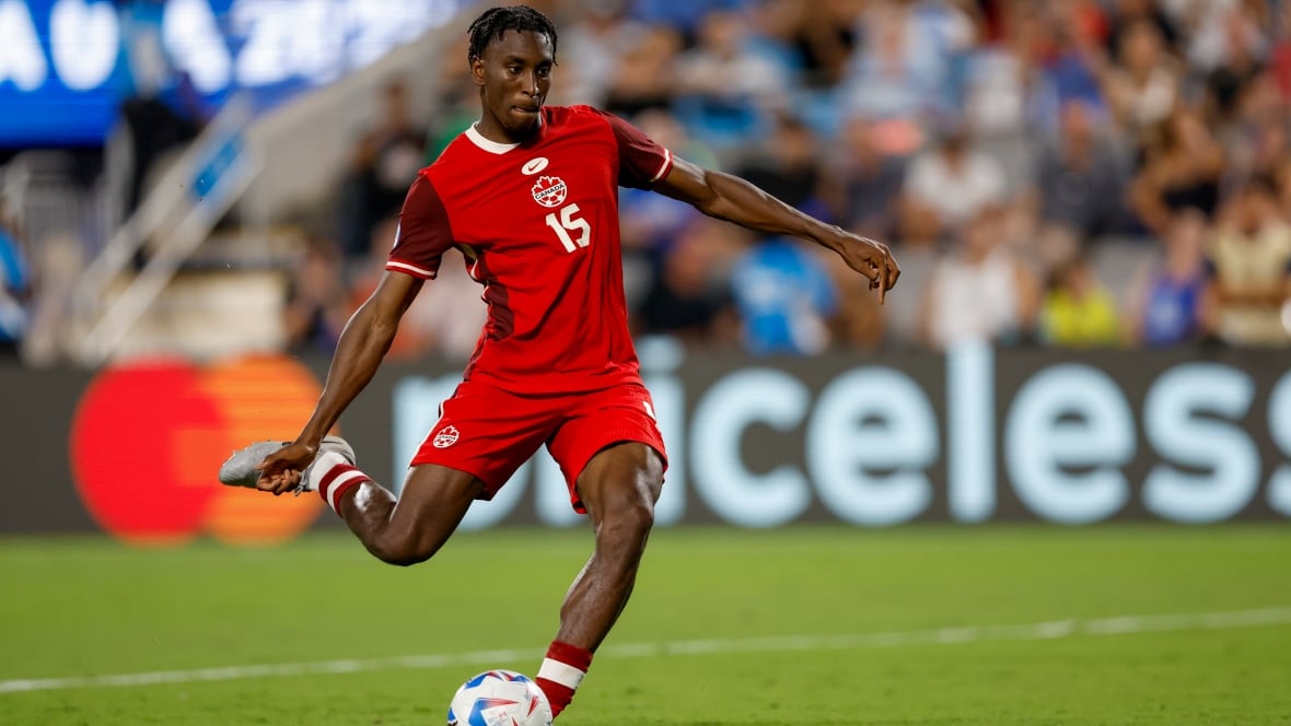 A male soccer player swings one leg back to kick ball during a penalty kick.