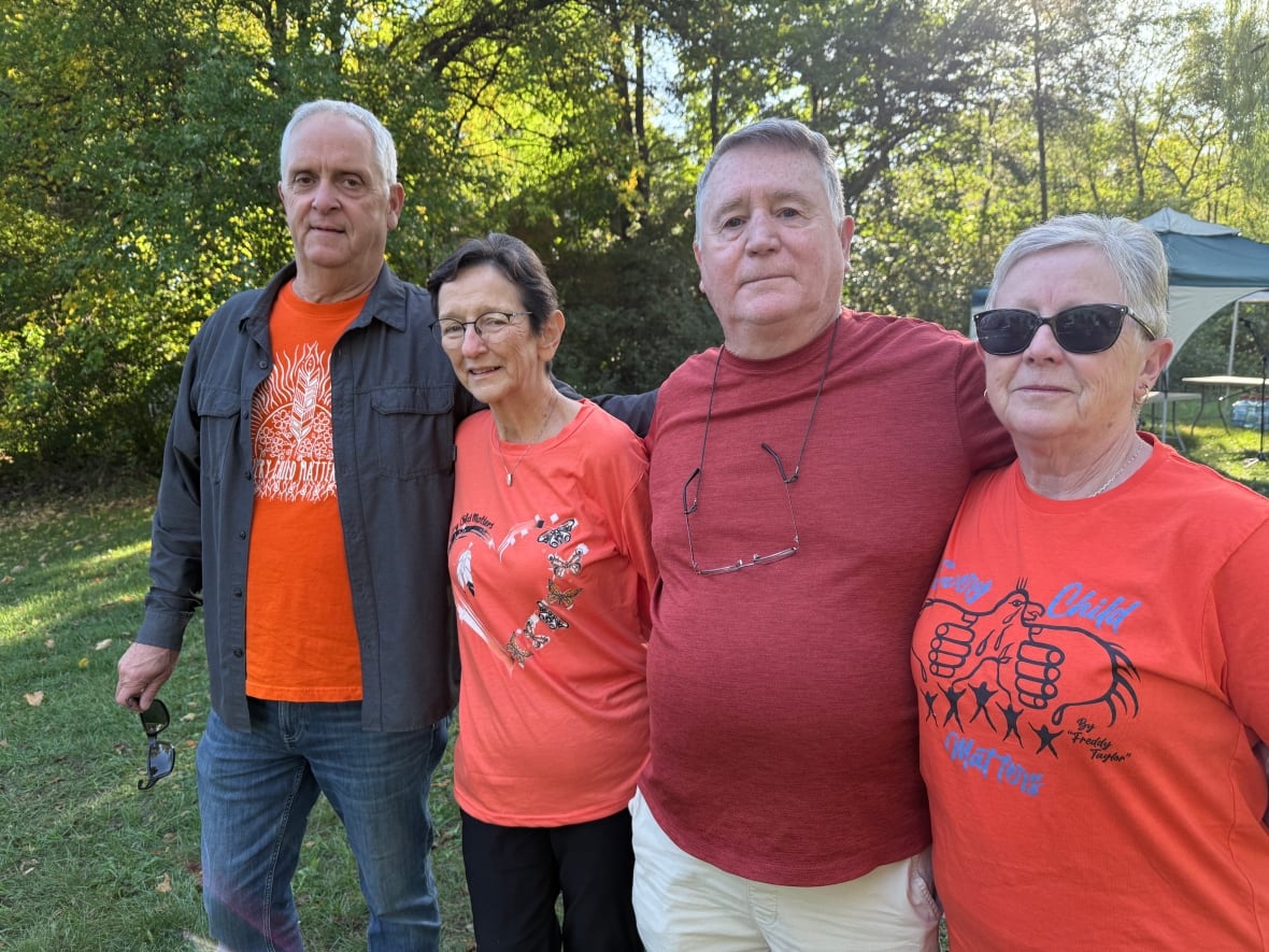 Four people in orange shirts pose arm in arm outside.