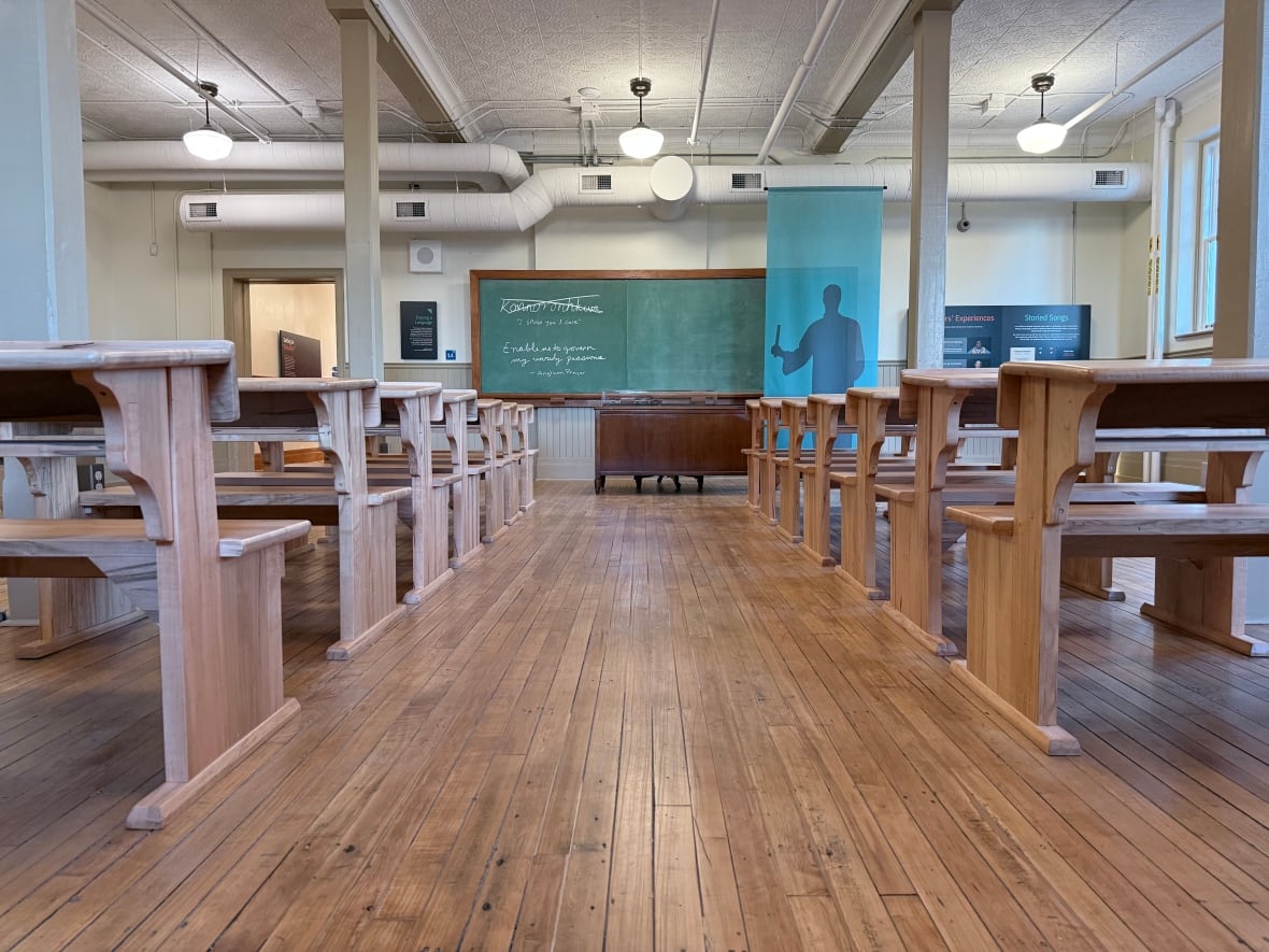 An old-style classroom set-up with a chalkboard and a cut-out of a teacher at the front.