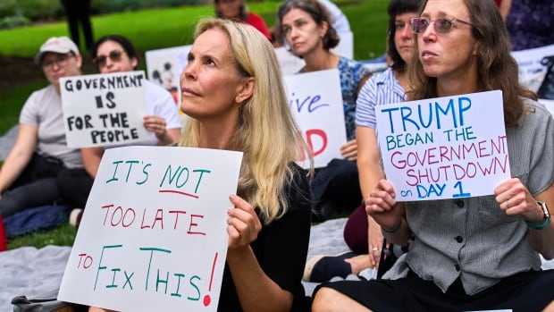Women sit on a  lawn holding protest signs