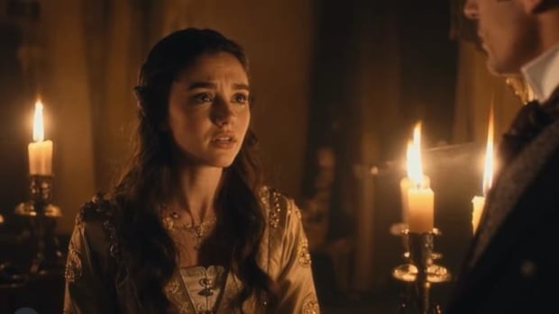 a woman in period era clothing is seen in candlelight, talking to a man whose side of his face is visible