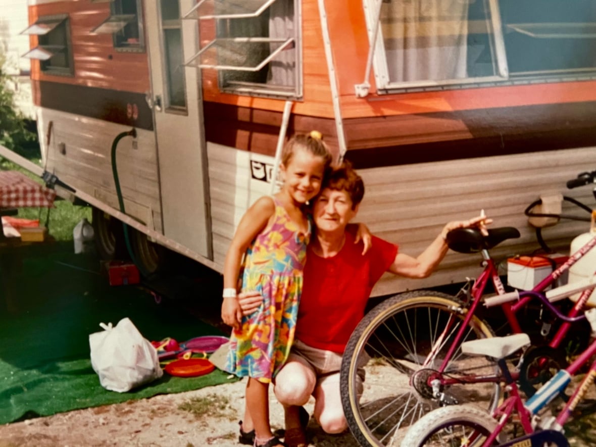 A faded family photo shows little girl posing with a middle aged woman outside a camper van next to children's bicycles.