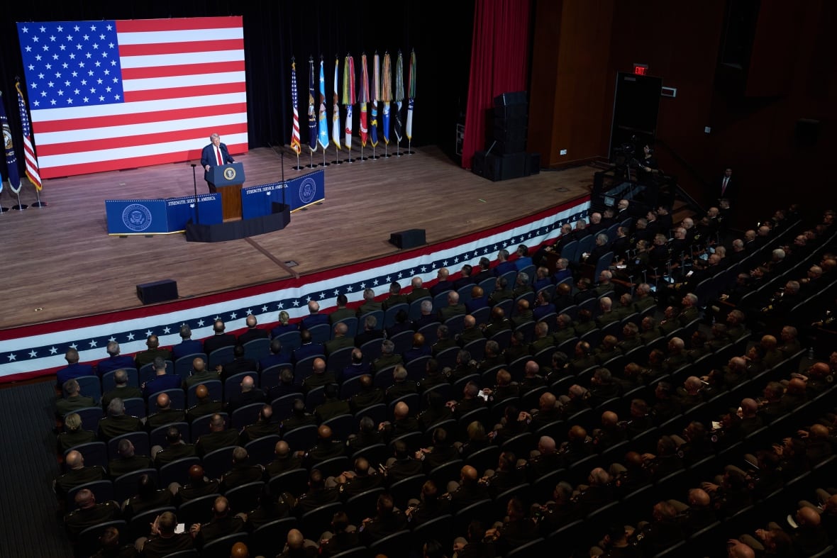 A man in costume talks about a podium in front of hundreds of soldiers sitting in a theater.
