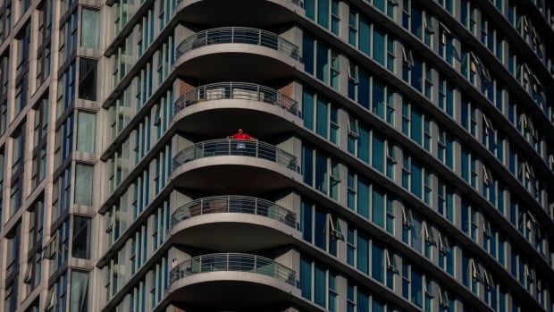 A man in a red shirt stands on a balcony in a condo building.