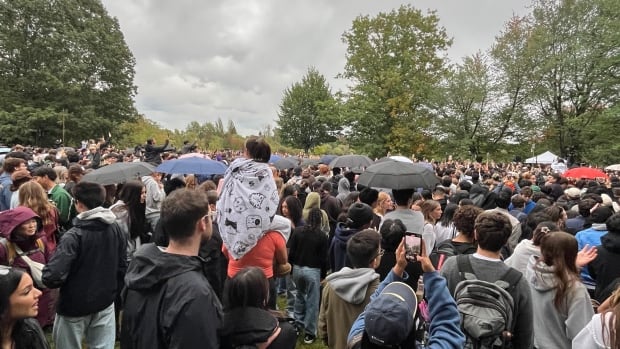 A crowd of people stand in a muddy field looking at a stage