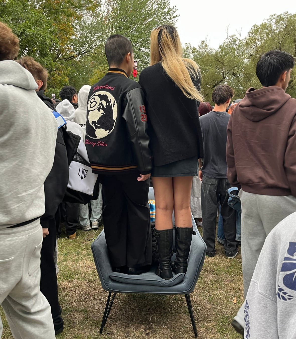 Two people stand on an armchair amid a crowd.