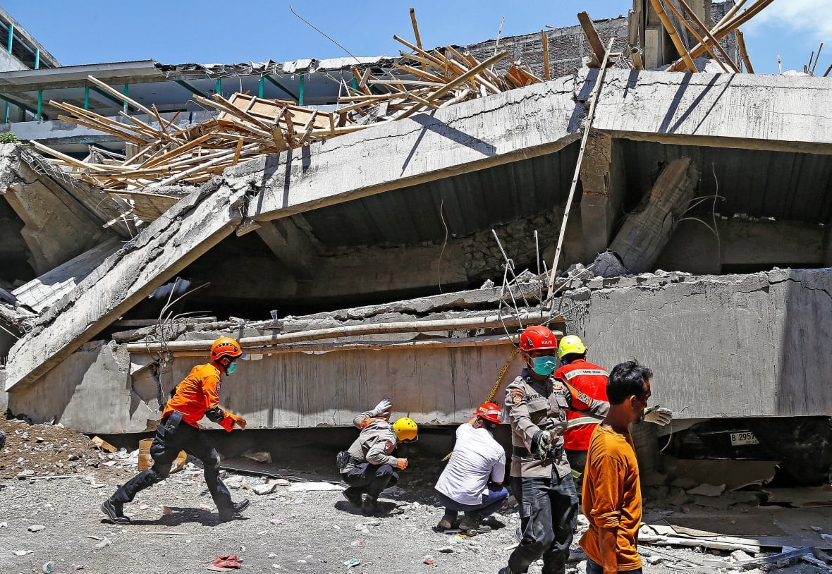 Half a scale of people are shown, some of them wear the uniform and the helmet near a large piece of concrete that collapsed near the ground.