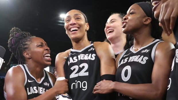 Four women's basketball players laugh and smile as they stand together.