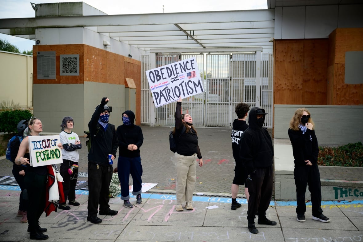 The demonstrators stand outside the gates building, with one person who holds a sign saying 
