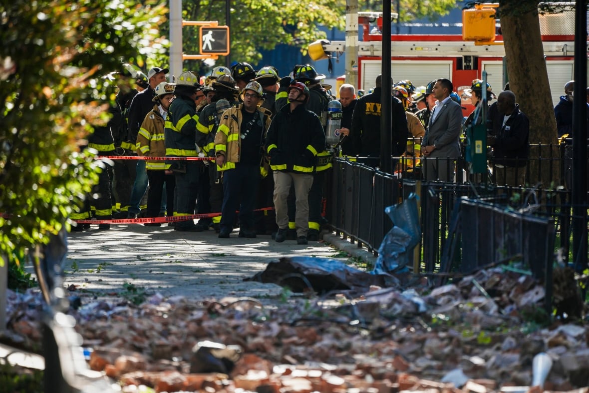 Firefighters are seen through next to a pile of bricks on the ground level of a highrise.